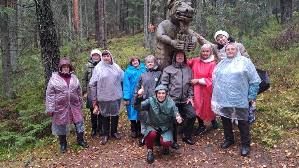 Projekto dalyviai prie medinės skulptūros