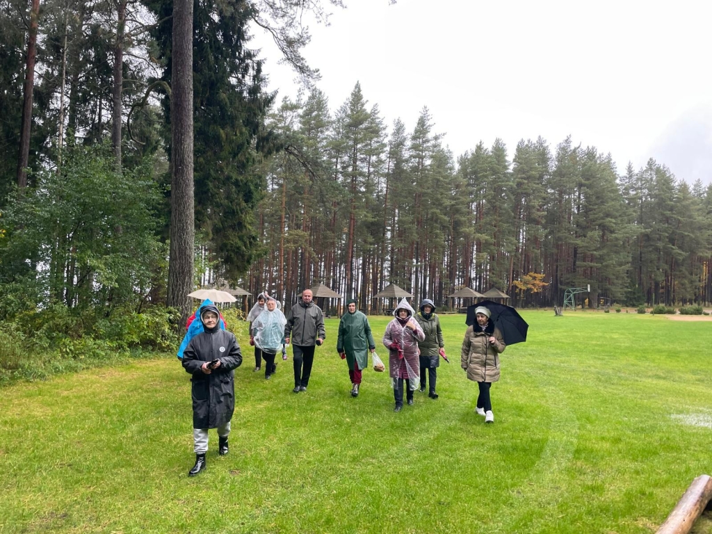 Projekto dalyvės vaikščioja pamiškėje su lietsargiais