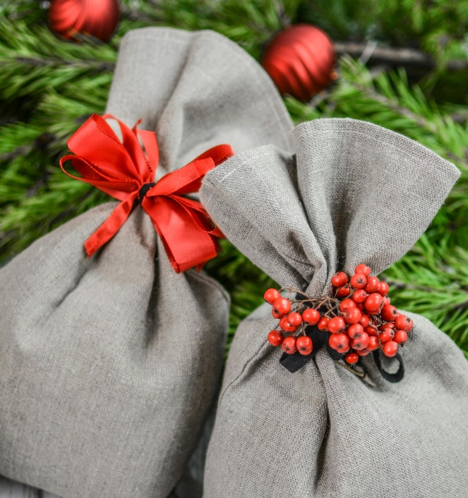 Du pilki drobiniai maišeliai su raudonais papuošimais: kaspinu ir šermukšnio uogomis