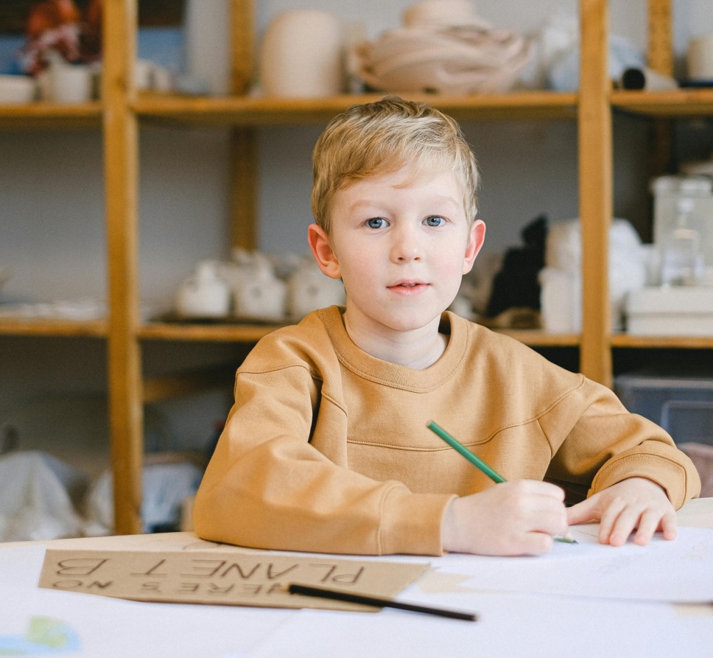 Berniukas rusvu megztiniu rašo ant balto popieriaus