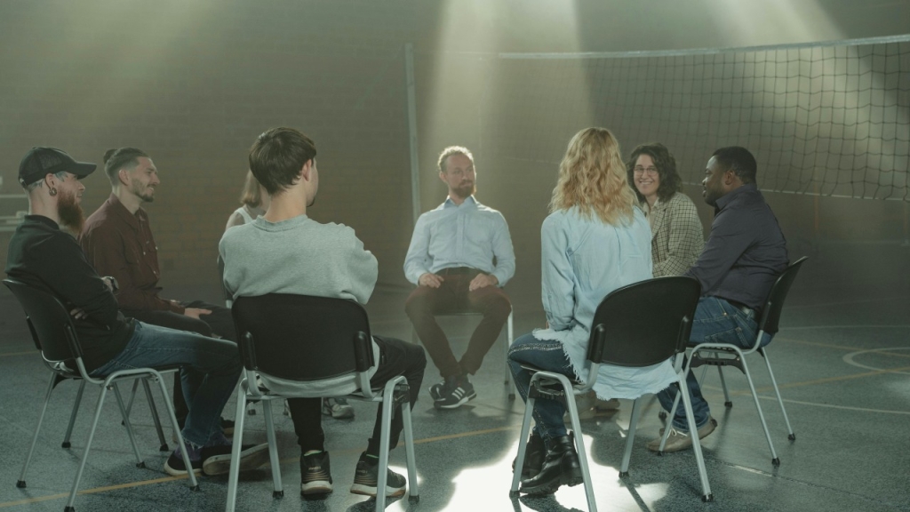 Žmonės sėdi ant kėdžių kambaryje