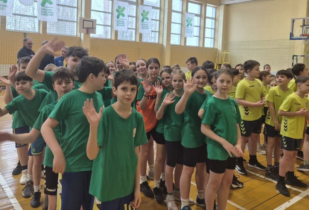 Mokiniai sporto salėje mojuoja prieš varžybų apdovanojimą.