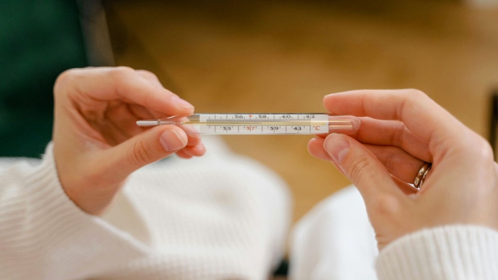 Žmogus, laikantis rankose stiklinį termometrą